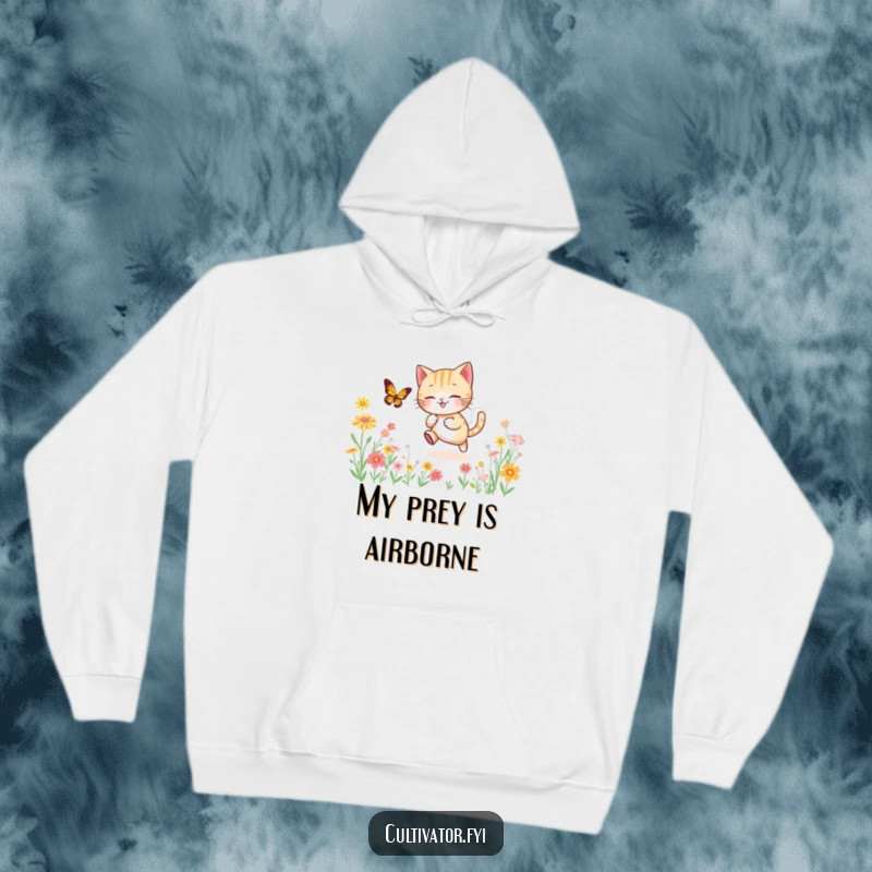 Funny, warm hoodie showing a lively cat playfully chasing a butterfly through a beautiful, sun-drenched field brimming with diverse flowers.